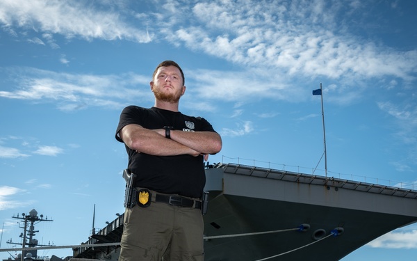 Naval Criminal Investigative Service (NCIS) Special Agent Afloat (SAA) Justin Botkin stand for an environmental portrait in front of the US Navy aircraft carrier USS Harry S. Truman (CVN 75) at Norfolk Naval Station Virginia on 19 September 2024.