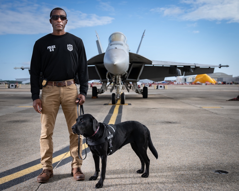 Naval Criminal Investigative Service (NCIS) Special Agent (SA) David Lawhorn and his K-9 companion Jill around the flight line with F-18 Hornets