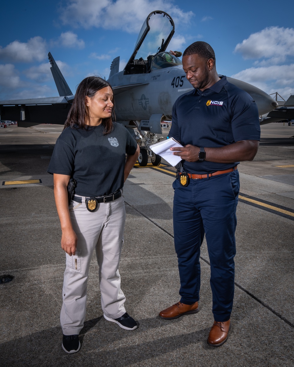 Naval Criminal Investigative Service (NCIS) Supervisory Special Agent (SSA) Jennifer Lynch and Special Agent (SA) Kenneth Randle discuss an on-going investigation around the flight line