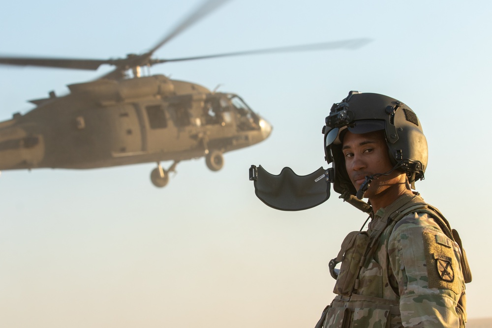 A Soldier Takes Off His Mask as a UH-60 Black Hawk Departs Behind Him