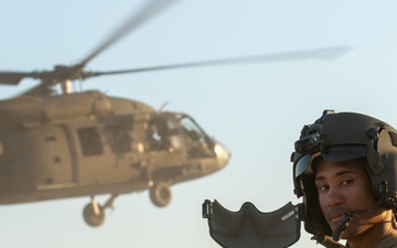 A Soldier Takes Off His Mask as a UH-60 Black Hawk Departs Behind Him