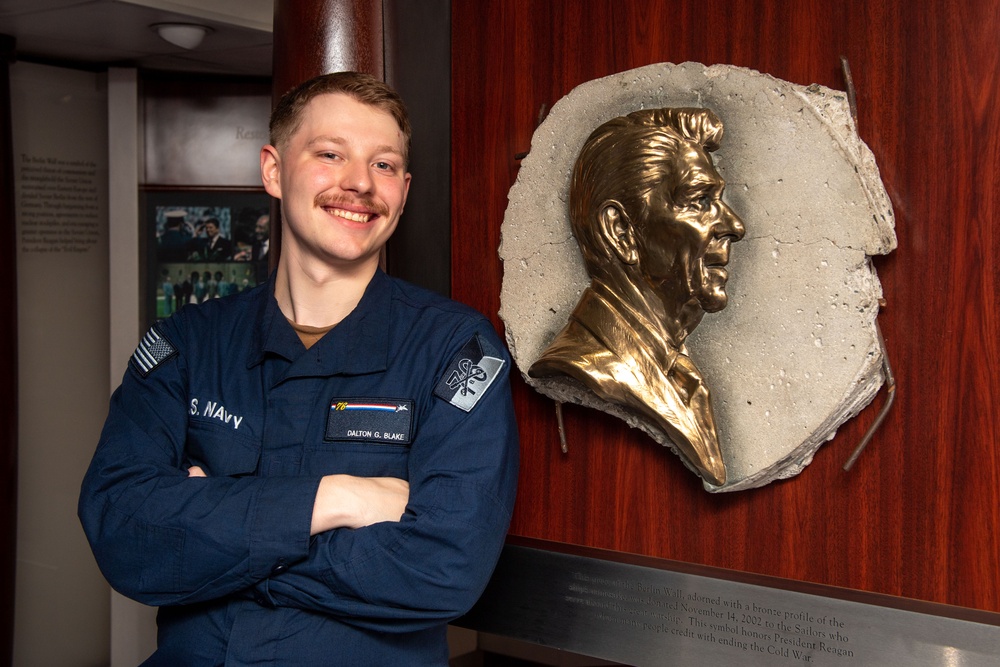 USS Ronald Reagan (CVN 76) Sailor poses with Ronald Reagan plaque