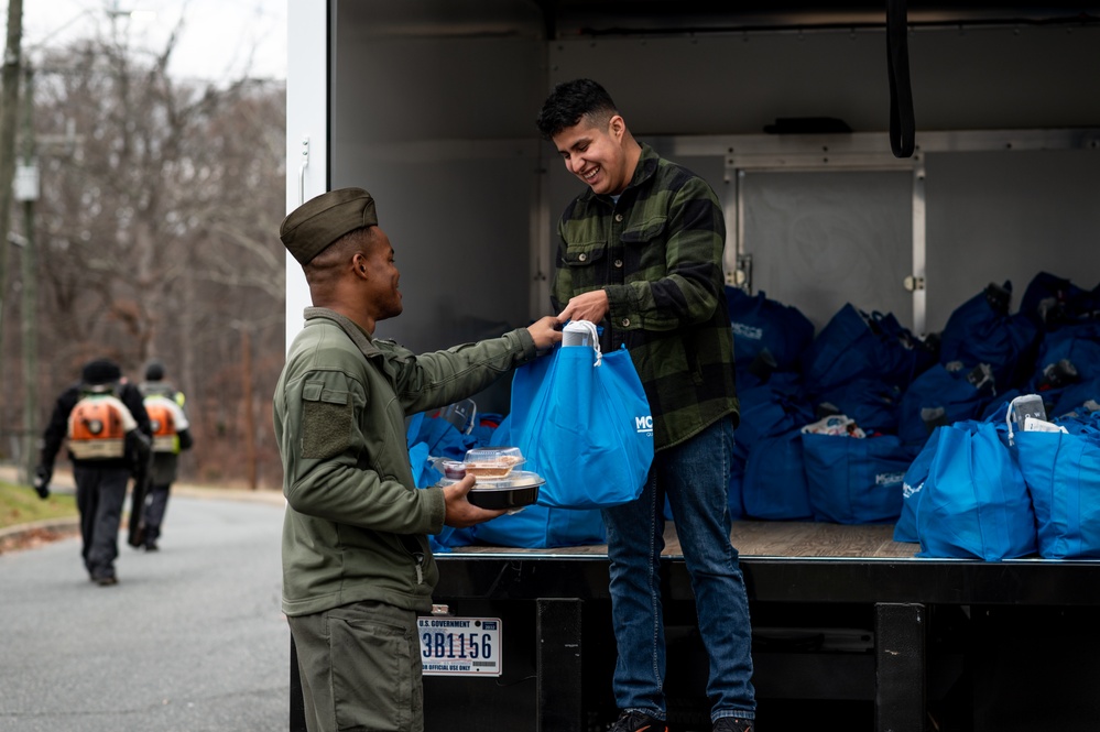 A volunteer hands a gift bag to a Marine at the Holidays in the Barracks event