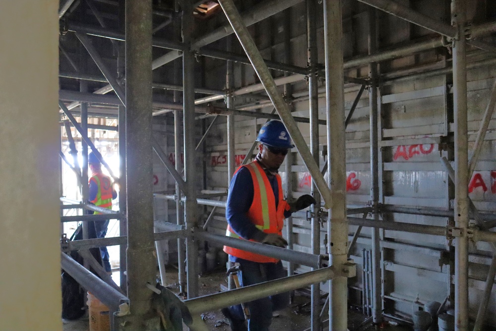 Construction workers navigate scaffolding in a hallway of Marine living quarters under construction