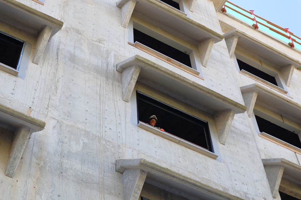 A construction worker smiles for the camera while working on the unfinished Bachelor Enlisted Quarters on Marine Corps Base Camp Blaz
