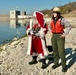 Santa Claus fishing while wearing a life jacket and standing next to USACE park ranger.