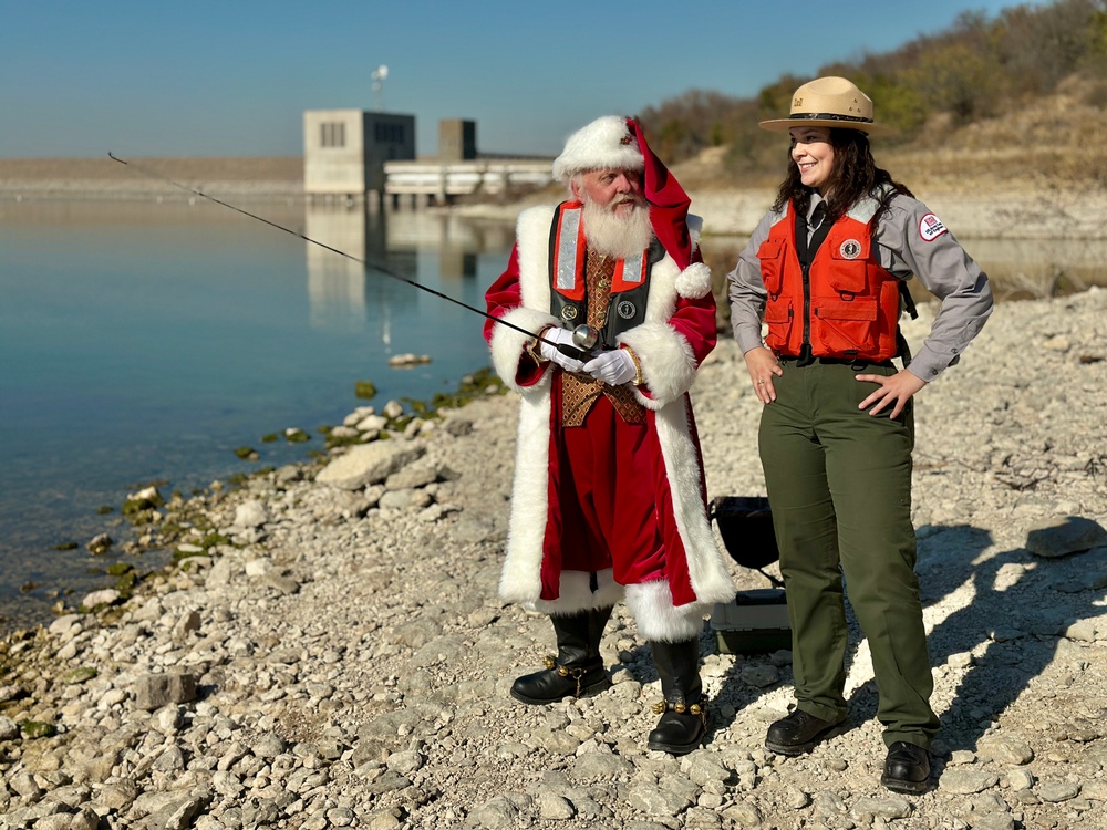 Santa Claus fishing while wearing a life jacket and talking to USACE park Ranger