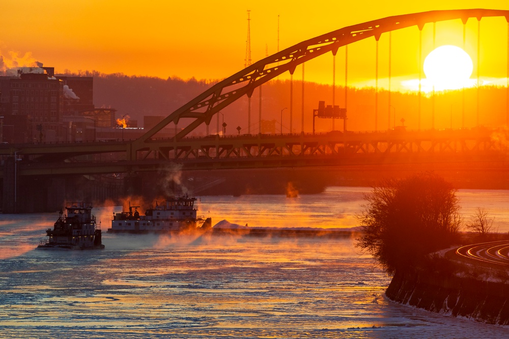 Sunfire and Ice: Towboats navigate through frozen rivers during Pittsburgh sunrise