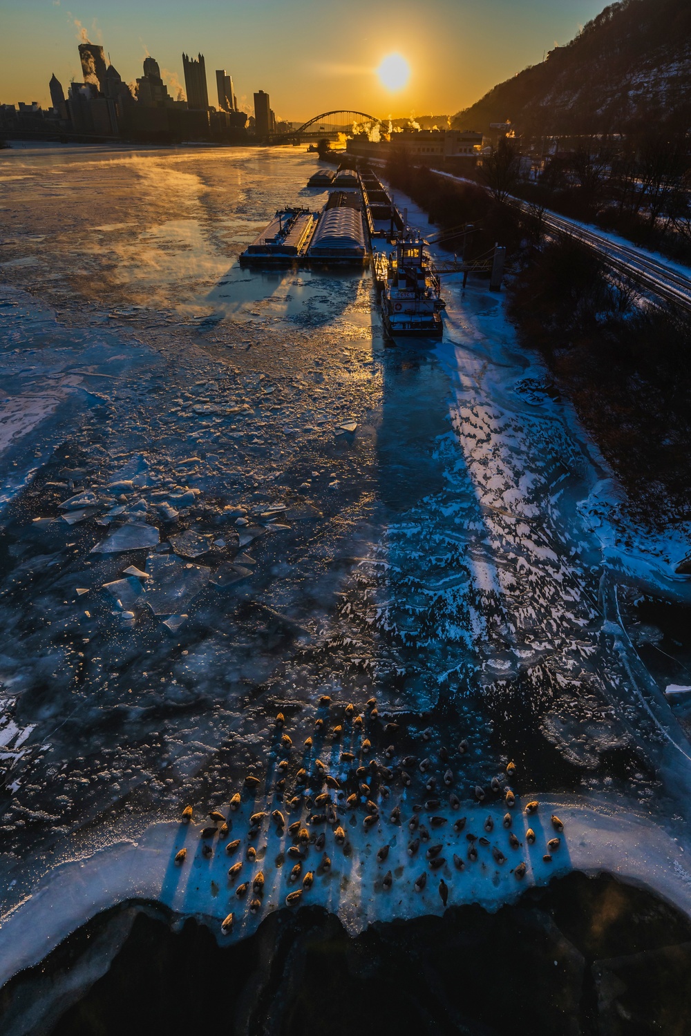 Sunfire and Ice: Towboats navigate through frozen rivers during Pittsburgh sunrise