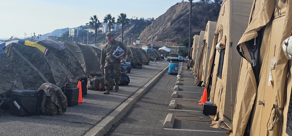 Soldier Walks along tents of other Soldiers camping at the Pacific Palisades