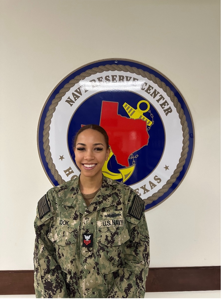 PS1 Cook stands in front of Navy Reserve emblem