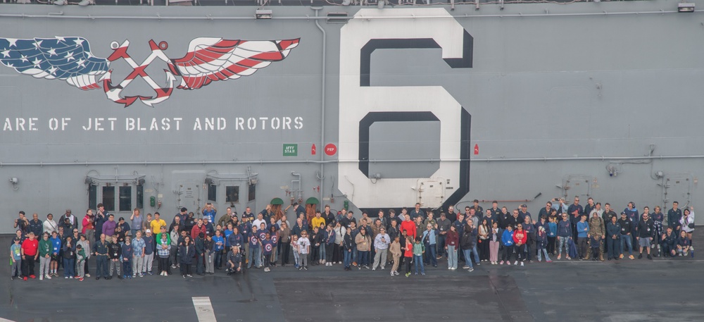 Sailors assigned to the USS America (LHA 6) and their families pose for a photo during a tiger cruise.