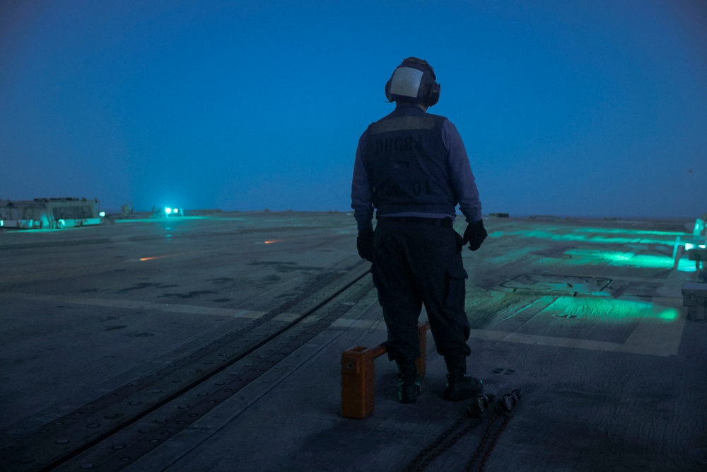 U.S. Navy Sailor stands ready to receive an approaching MH-60R Seahawk helicopter on the aft flight deck of the USS Bulkeley.