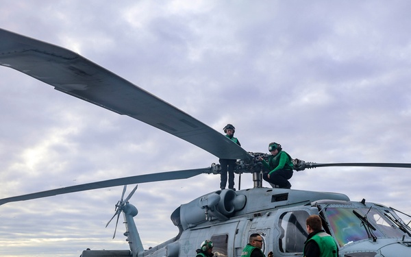 Ground crew conduct pre-flight checks on a MH-60R Sea Hawk helicopter.