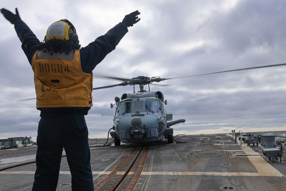 Boatswain Mate 2nd Class Jalynn Simons signals to the MH-60R Sea Hawk helicopter pilots