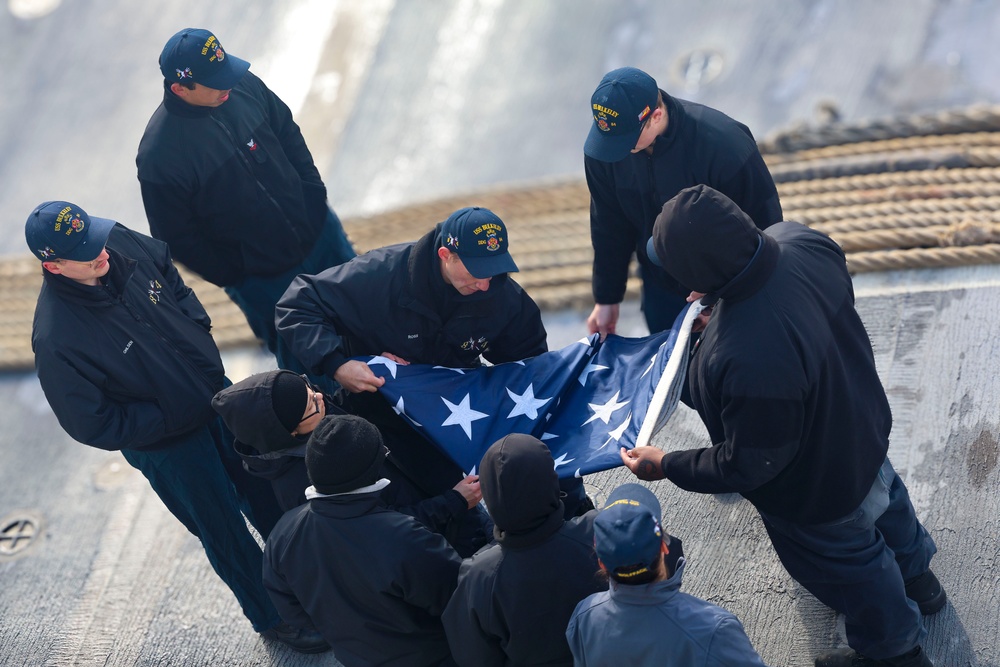 U.S. Navy Sailors fold the ensign during a sea-and-anchor detail