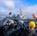 Cmdr. Arturo Trejo and and U.S. Navy Sailors wave to  the crew onboard the USS Thomas Hudner (DDG 116)