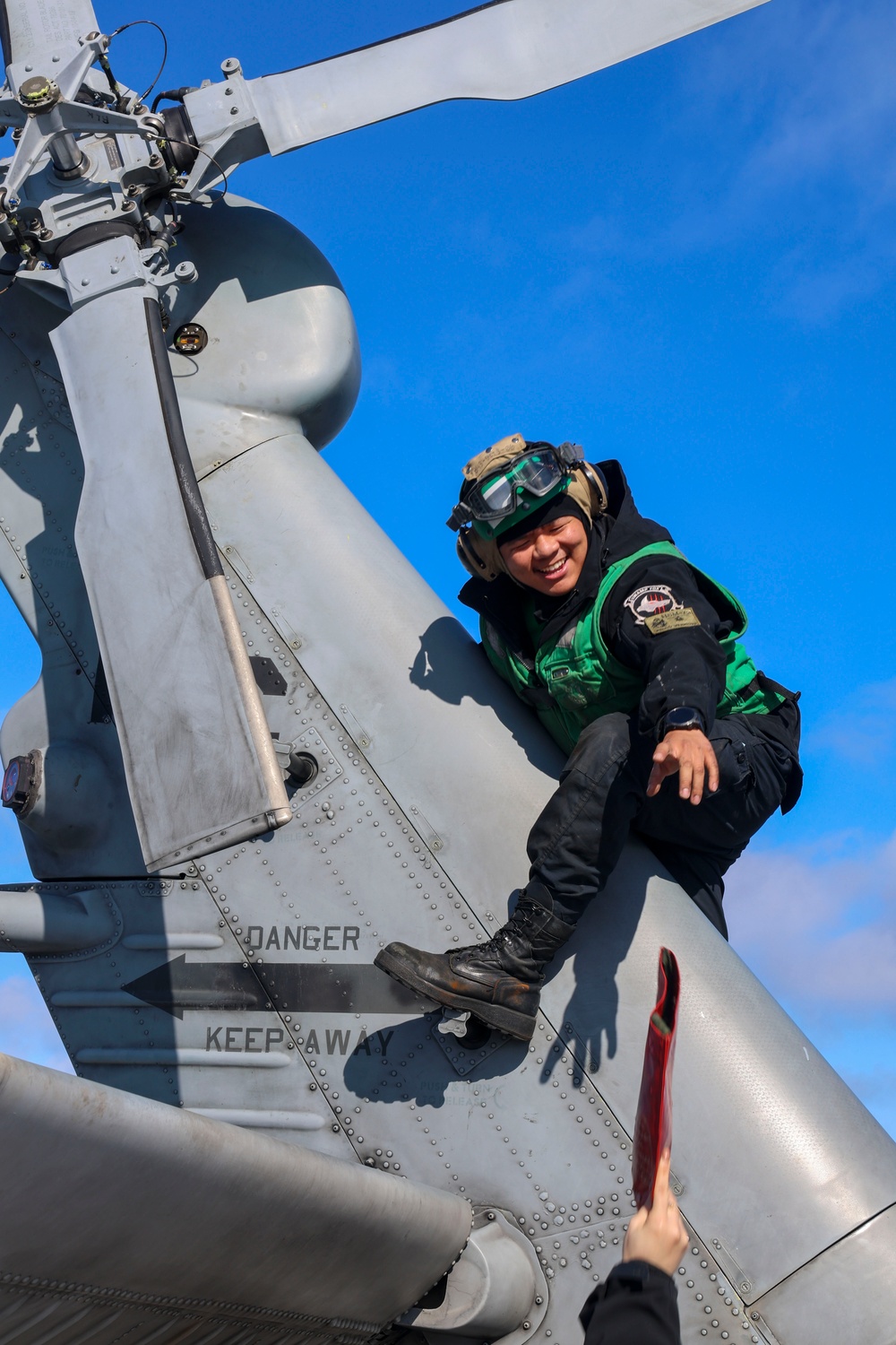 Aviation Machinist’s Mate 2nd Class Keith Gonzales receives a tail rotor blade cover to install on the tail rotor prior to stowing a MH-60R Sea Hawk helicopter