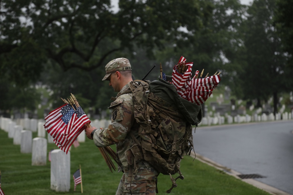 A Soldier from the 3d U.S. Infantry Regiment (The Old Guard) places American flags at headstones during “Flags In” at Arlington National Cemetery, Arlington, Va., May 22, 2025.