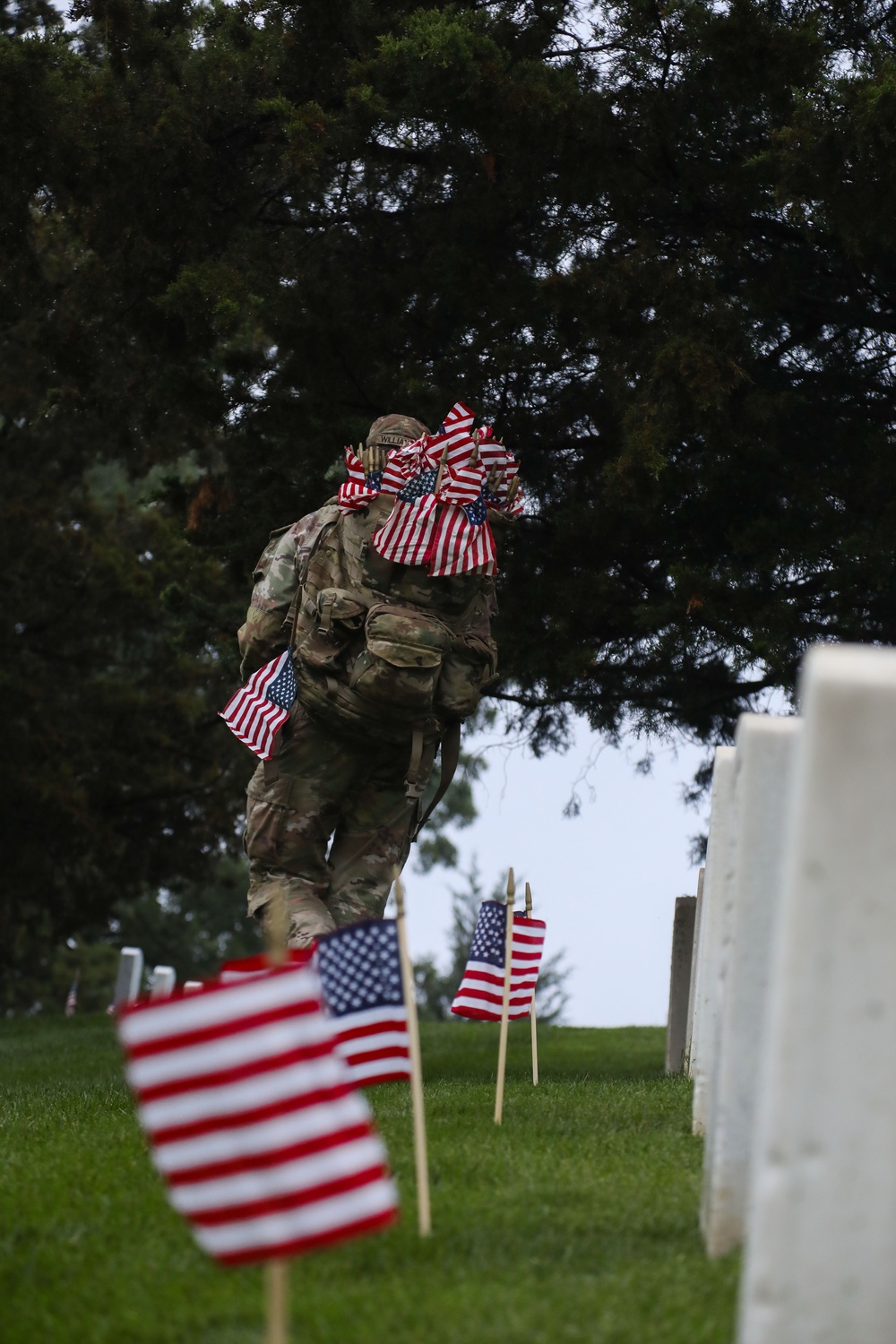 A Soldier from the 3d U.S. Infantry Regiment (The Old Guard) places American flags at headstones as part of &quot;Flags In&quot; at Arlington National Cemetery, Arlington, Va., May 22, 2025.