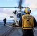 BM1 Jason Carpenter signals to the MH-60R Sea Hawk helicopter pilot