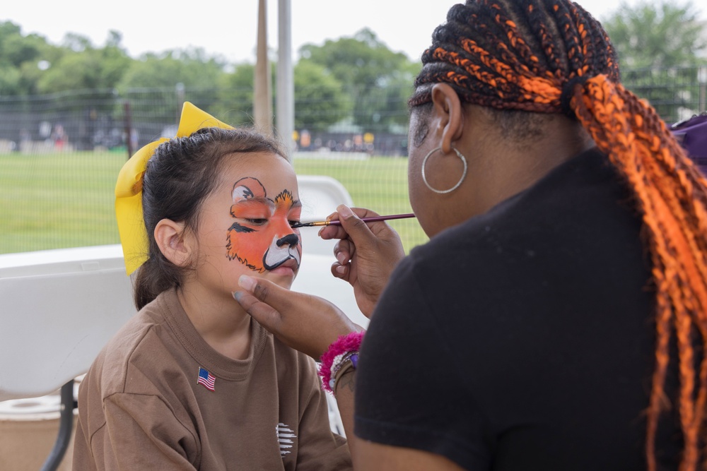 A volunteer paints a little girl's face with an animal design at the 250th U.S. Army Birthday Festival