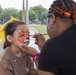 A volunteer paints a little girl's face with an animal design at the 250th U.S. Army Birthday Festival