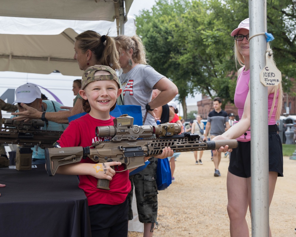 A little boy carefully handles a display weapon with his mother at the 250th U.S. Army Birthday Festival
