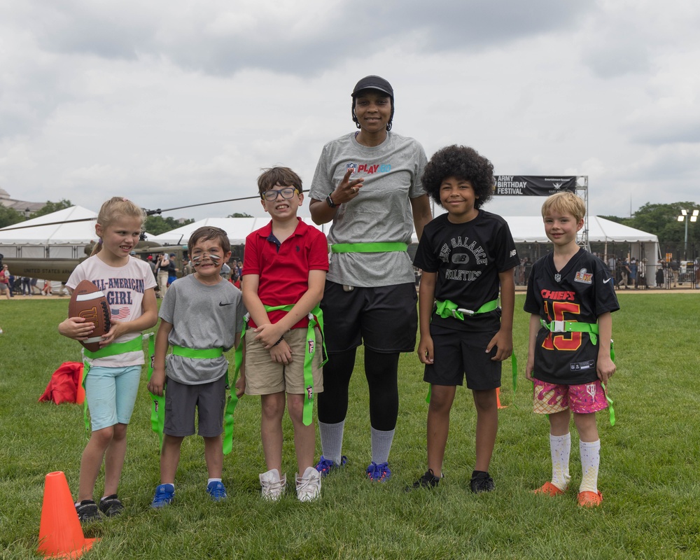 A coach poses with children to play flag football at the 250th U.S. Army Birthday Festival