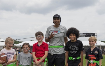 A coach poses with children to play flag football at the 250th U.S. Army Birthday Festival