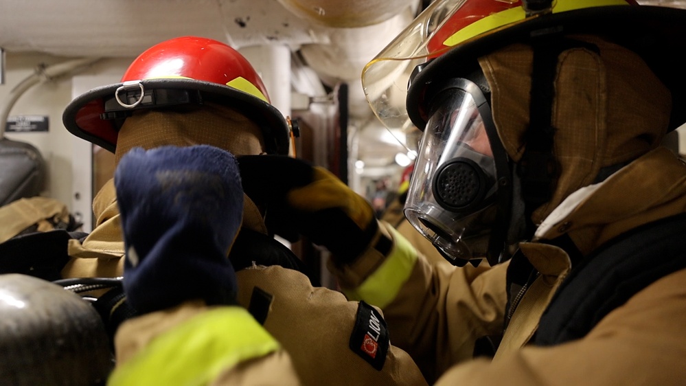 DC3 Luke Bryant assists another sailor with fitting firefighting gear