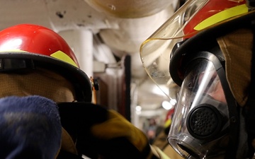 DC3 Luke Bryant assists another sailor with fitting firefighting gear