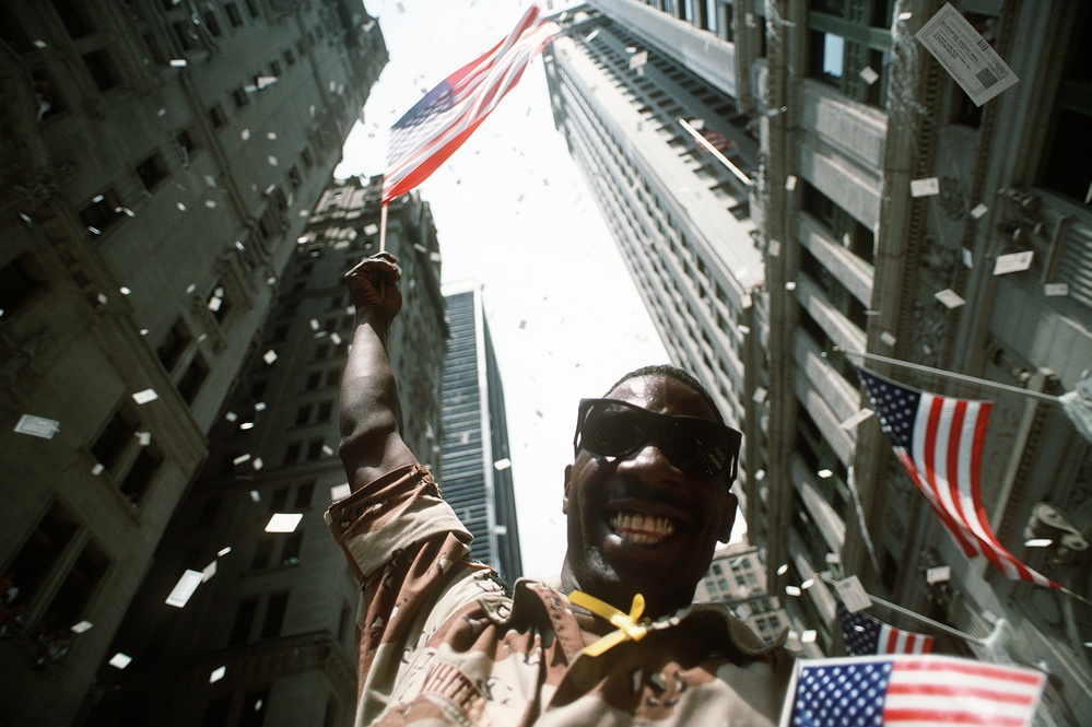 Triumphant Homecoming: Soldier Waves Flag at Desert Storm Victory Parade