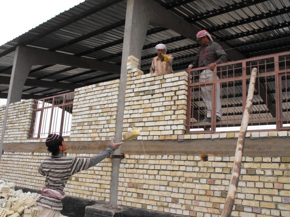 Iraqi Worker Tosses Brick During School Supply Warehouse Construction in Baghdad