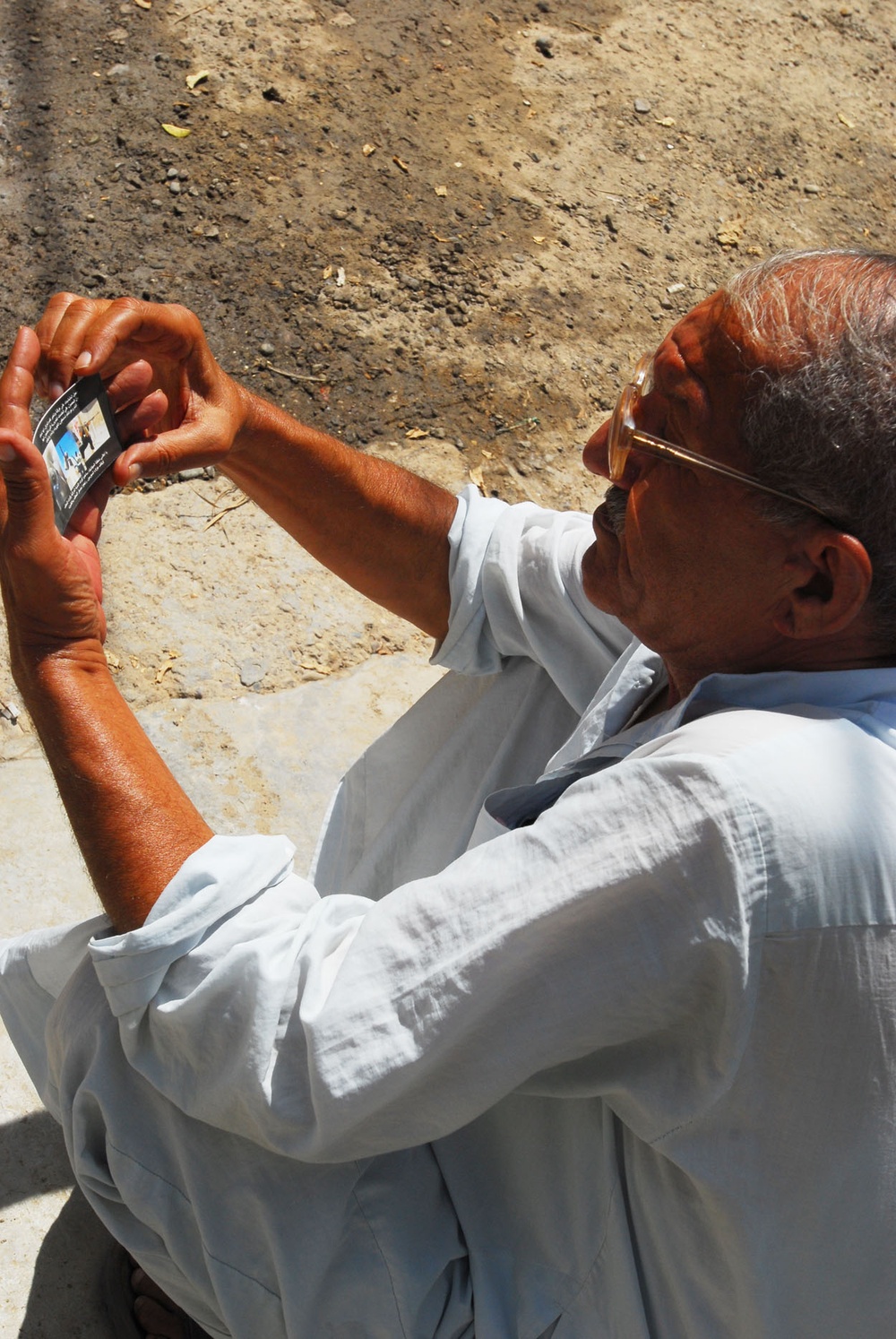 Iraqi Citizen Reads from Tip Hotline Card as Soldiers Provide Security for Returning Families