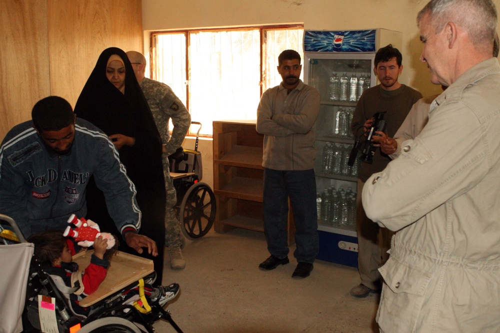 Oliver North Visits Iraqi Child Receiving Wheelchair at Radwaniyah Palace Complex
