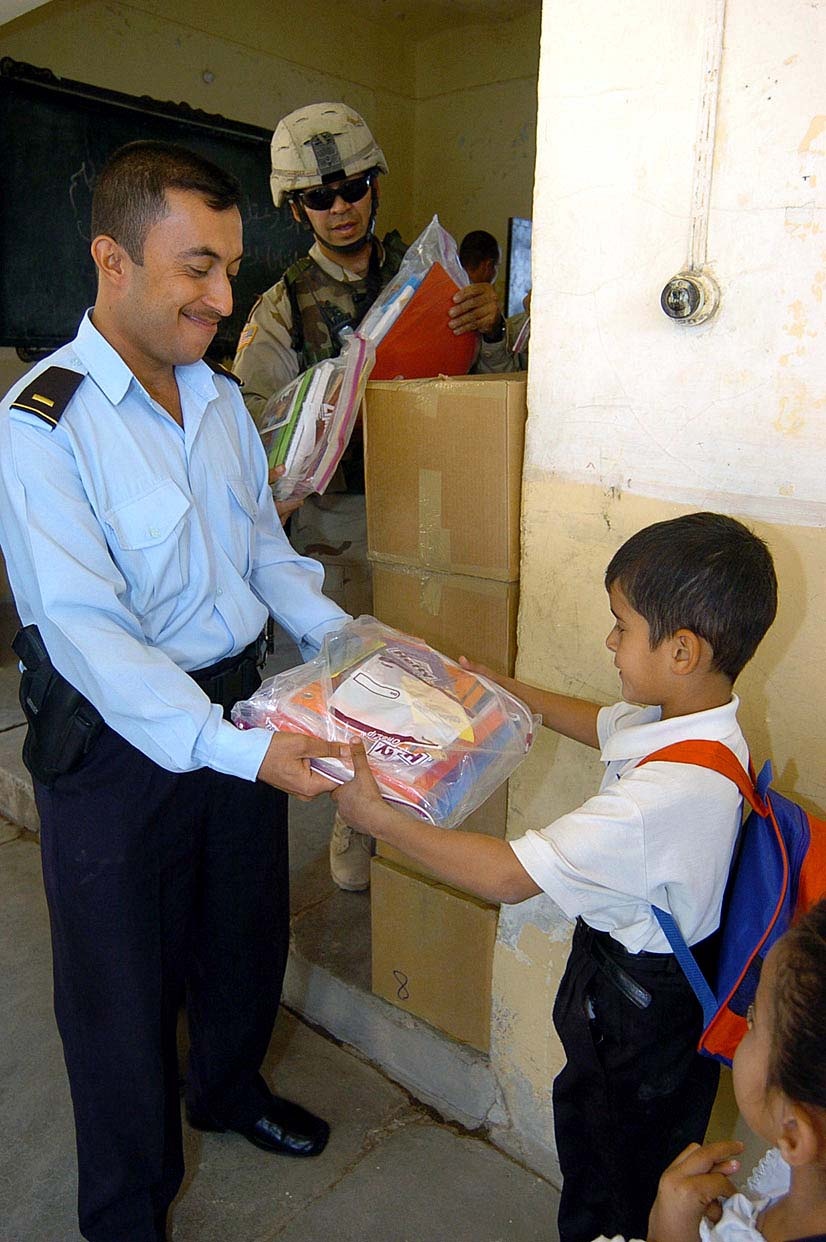 Iraqi Police Officer Distributes School Supplies to Students with U.S. Army Support