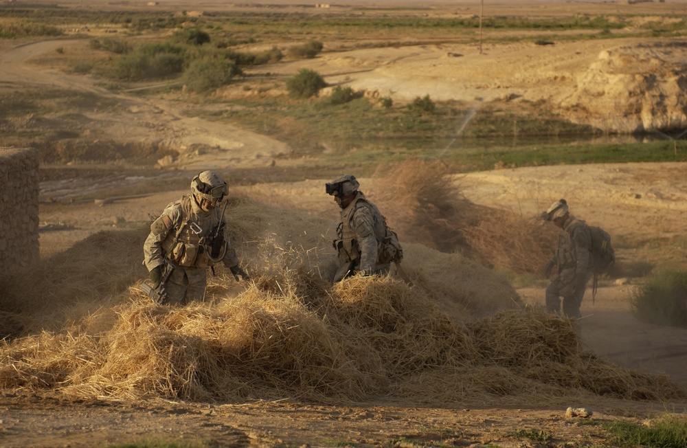 Soldiers Search Haystack for Weapons Cache in Iraq