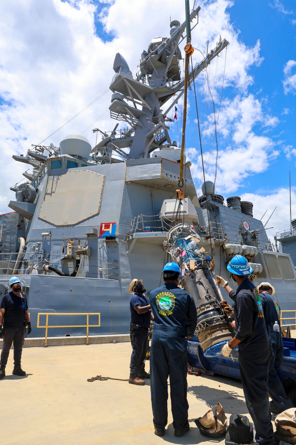 Sailors and contractors connect an Allison gas turbine generator to a crane hoist for loading