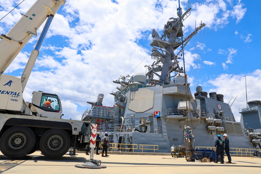 Sailors and contractors load a turbine generator to a crane hoist for loading