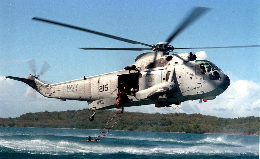 U.S. Navy Sea King helicopter hovers over the water to recover EOD technicians.