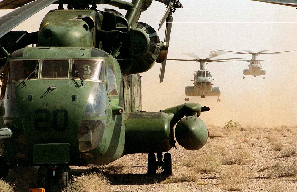 CH-46 Sea Knights stir up a cloud of dust as they launch behind a CH-53 Sea Stallion.