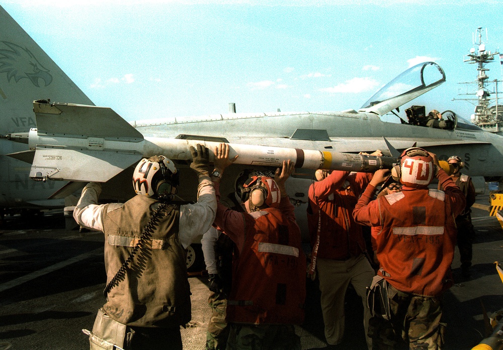 Aviation ordnancemen load an AIM-9 Sidewinder short range missile on an F/A-18 Hornet.