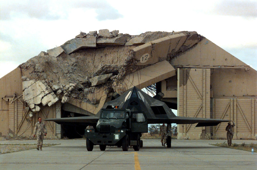An F-117A Nighthawk is towed in front of a destroyed aircraft shelter at Ahmed Al-Jaber Air Base.