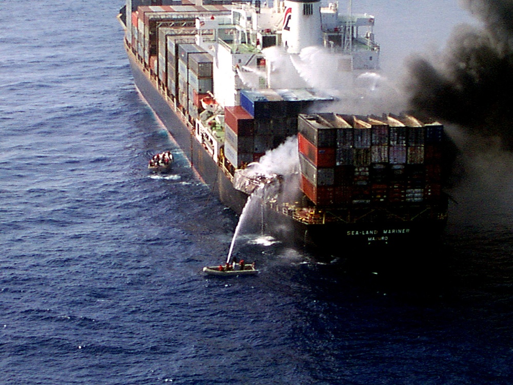 Sailors from the USS Wasp aim a fire hose at burning cargo containers aboard the Sea Land Mariner.