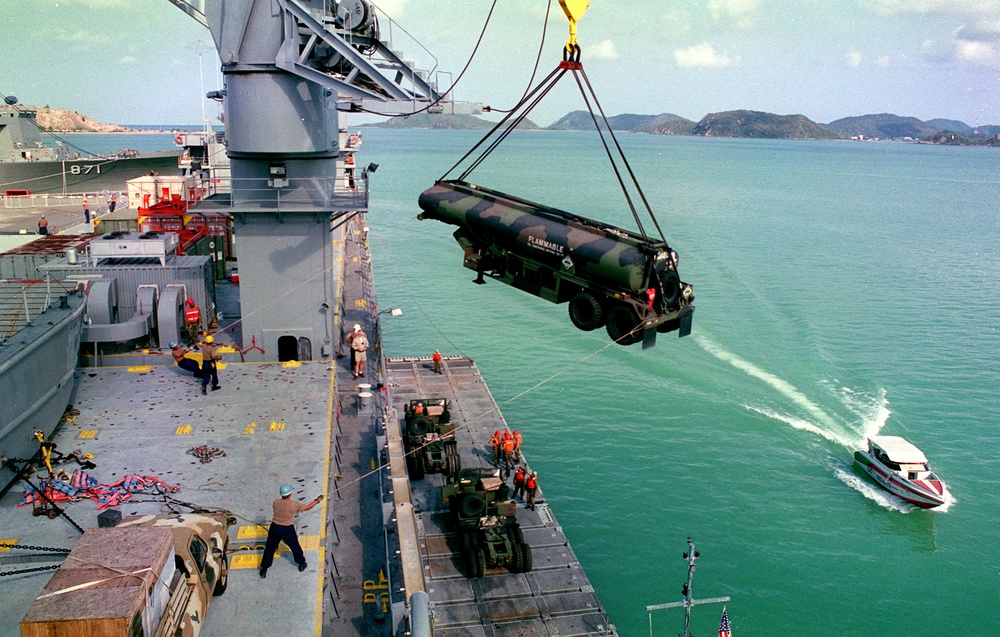 Sailors and Marines guide a tanker trailer as it is lowered to a lighter craft in Sattahip, Thailand.