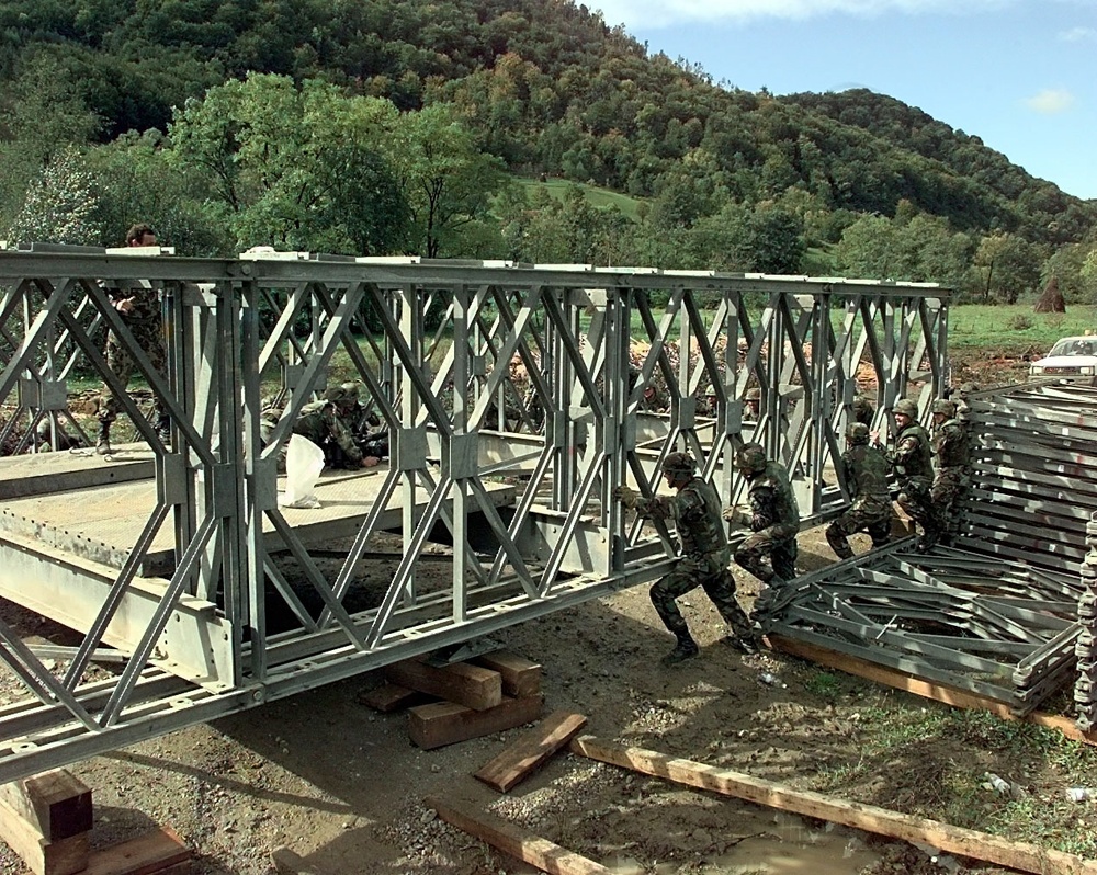 Army engineers use their brute strength to push a partially constructed bridge into position