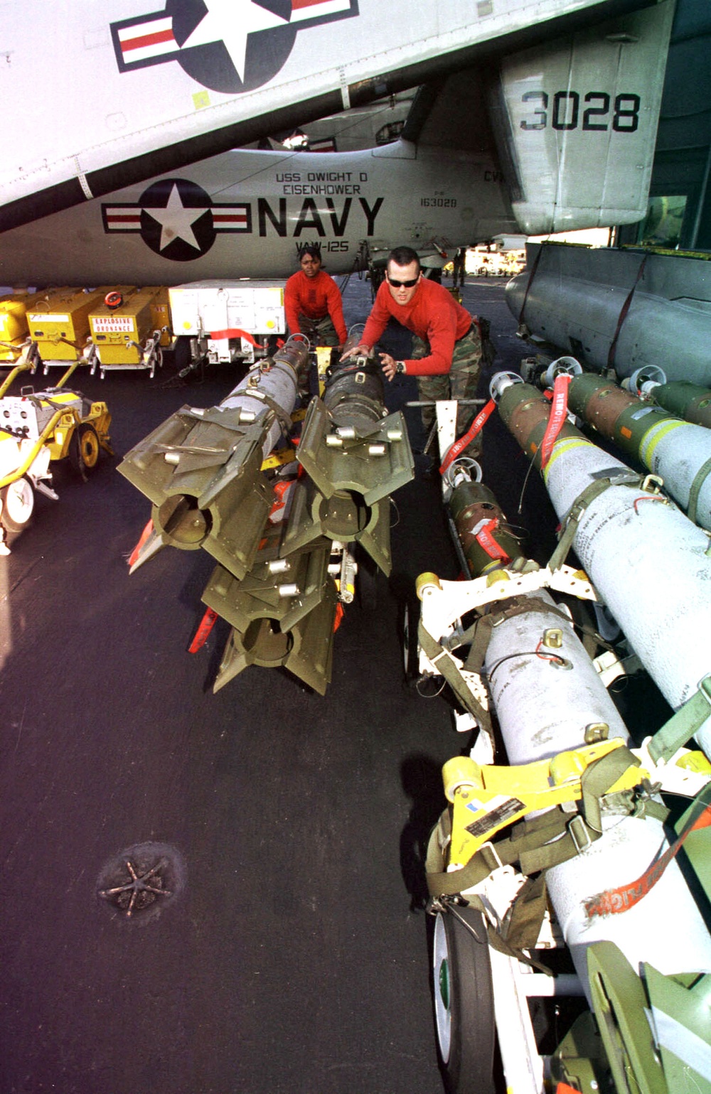 Aviation ordnancemen push a cart of GBU-16 bombs on the USS Dwight D. Eisenhower.