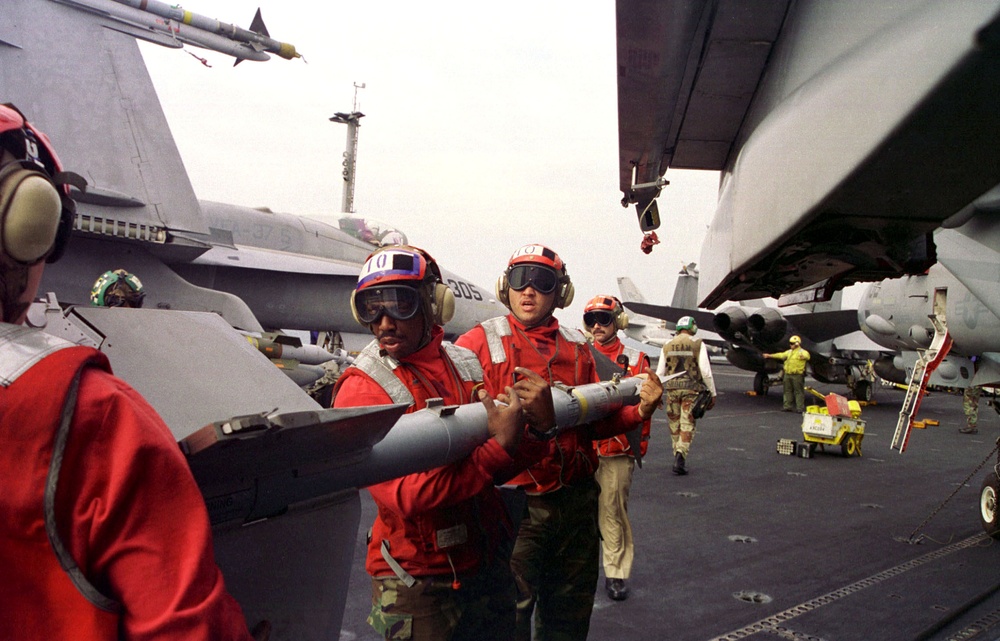 Aviation ordnancemen use teamwork and brute strength to load an AIM-9M Sidewinder.