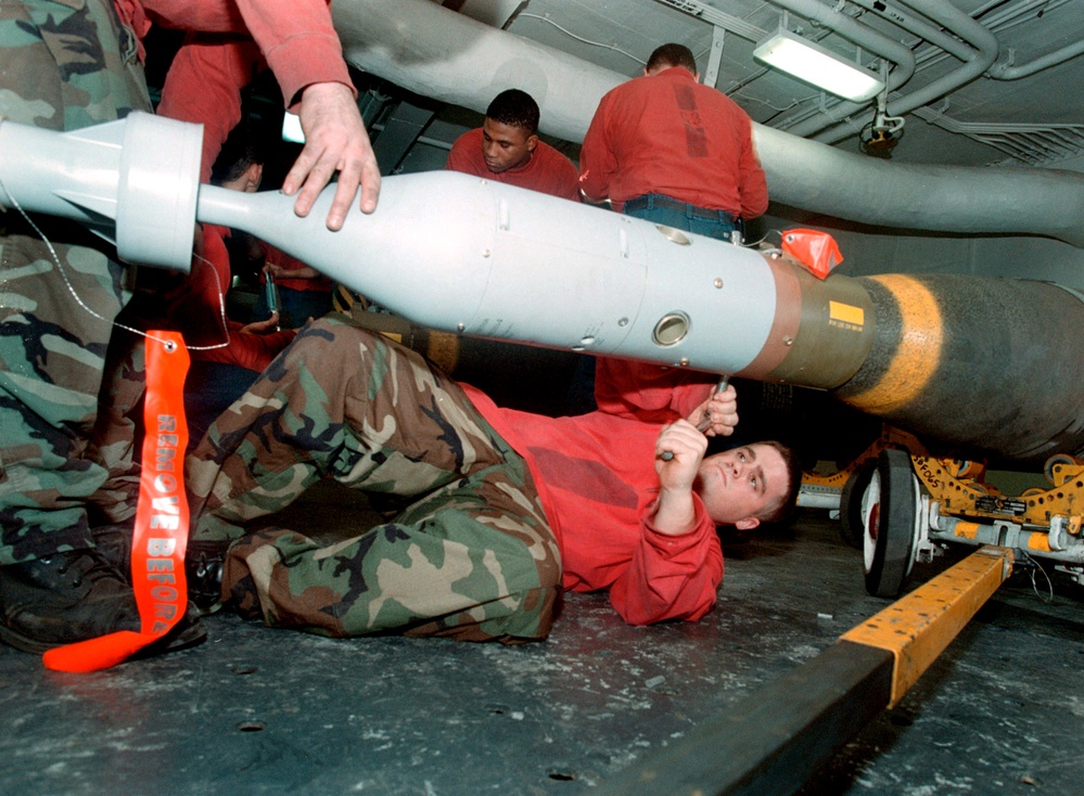 An aviation ordnanceman tightens a laser guiding device to the nose of a 2,000 pound bomb.